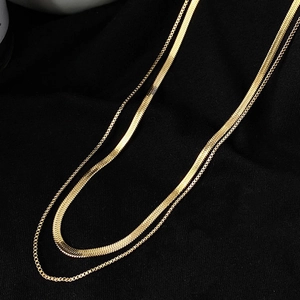 Elegant gold double-layer necklace with fine box chain and flat snake chain over black fabric