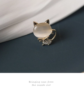 Détail d'une broche chat dorée avec pierre œil-de-chat et strass brillants sur tissu