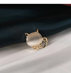 Détail d'une mignonne broche chat dorée avec pierre œil-de-chat et nœud orné de zircons