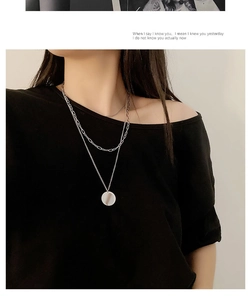 Detail of silver double-layered necklace with round polished pendant on black clothing