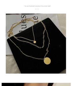 Detail of a layered gold necklace with circular pendants on a black luxury gift box