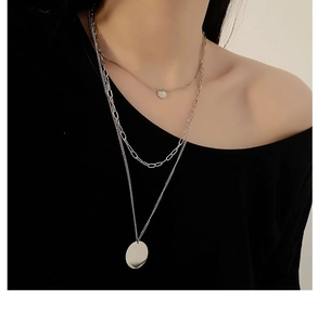 Close-up of a three-layered silver layered necklace featuring circular pendants and paperclip links