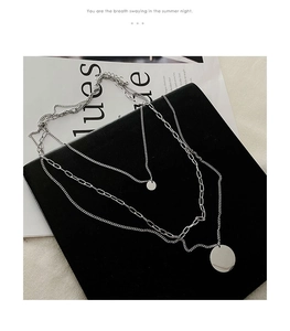 Detailed view of triple-layered silver necklace with circular pendants and paperclip chains