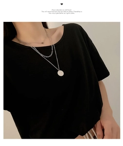 Close-up of triple-layered silver necklace with round pendant on black top