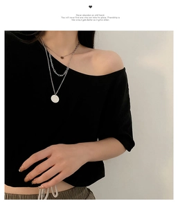 Close-up of triple-layered silver necklaces with circular pendants on black clothing