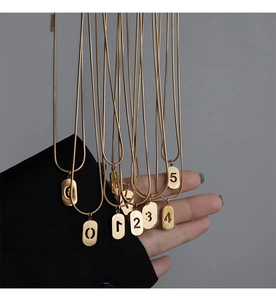 Détail de plusieurs colliers en maille serpent dorée avec pendentifs numérotés à la main
