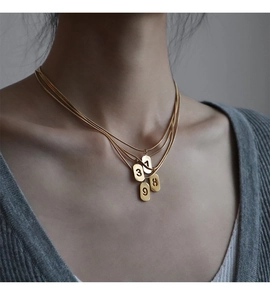 Détail de colliers multicouches dorés avec pendentifs chiffres sur un pull gris chic