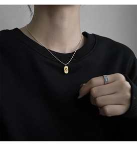 Détail d'un collier doré avec pendentif numéro 9 et bague large en argent épurée