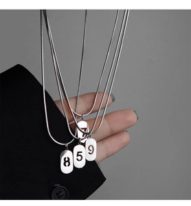 Détail de chaînes serpent argentées avec pendentifs ovales ajourés montrant les chiffres 8, 5, 9, 7