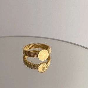 Vintage golden coin ring with Elizabeth II portrait and woven metal band on reflective surface