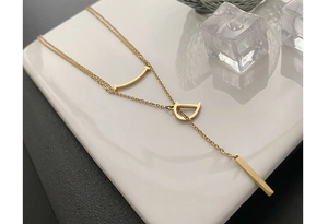Détail d'un collier doré double épaisseur avec pendentif D et barre sur plateau en céramique