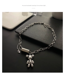 Détail d'un pendentif ours argenté sur une chaîne épaisse avec petite étiquette Luck