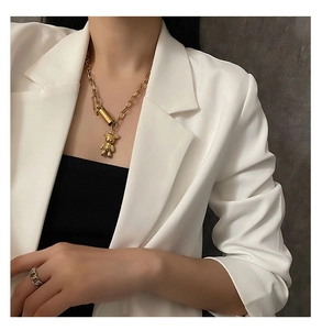 Gros plan d'un collier chaîne dorée avec pendentif ours et bague tressée argentée