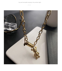 Gros plan du collier ours doré avec breloque LUCKY sur support en céramique blanche