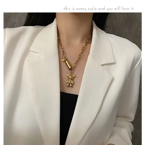 Détail d'un collier avec pendentif ours doré et chaîne épaisse sur un blazer blanc