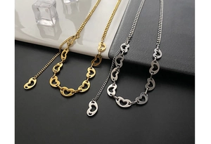 Detail of heart-shaped hollow link chains in gold and silver finish on a textured background