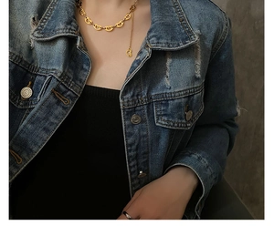 Close-up of golden heart link necklace worn with a vintage distressed denim jacket