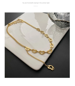 Detail of gold heart-shaped Y-necklace with layered links and pendant on white ceramic tray