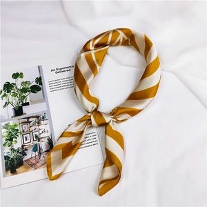 Detail of striped silk square scarf tied in a neat knot on white textured fabric