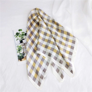 Detailed flat lay of a yellow and grey checkerboard silk scarf on textured fabric
