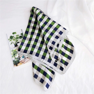 Detail of checkered square silk scarf with deep green and navy patterns on soft fabric