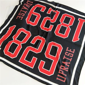Detail of square scarf featuring red numeric print and UPRAISE text on black fabric