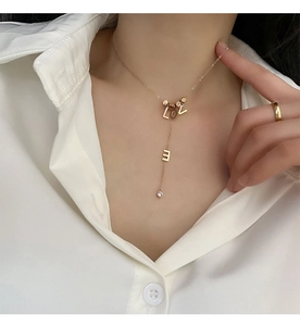 Detail of gold LOVE titanium necklace with rhinestone pendant on female model