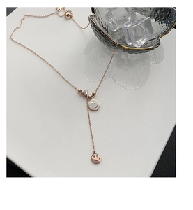 Gros plan d'un pendentif sourire en or rose et chaîne à perles sur fond glacé pur