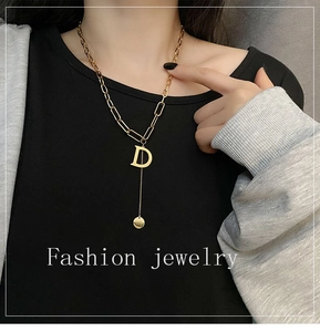 Detail of a long gold titanium steel G-pendant necklace on a black sweater background