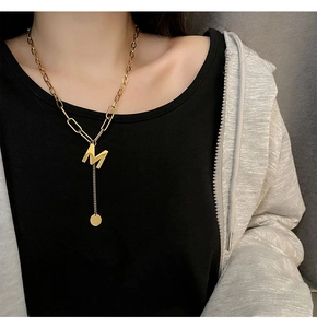 Detail of gold-plated M letter pendant on mixed link chain necklace worn by model