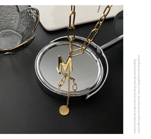 Macro shot of gold letter M pendant with chunky paperclip chain and tassel disc