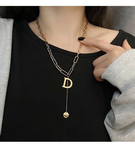 Detail of gold letter D pendant necklace with sleek metal disc on a model with black top