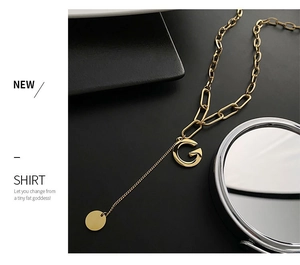 Detail of gold titanium steel G letter pendant with asymmetric chain and round disc charm