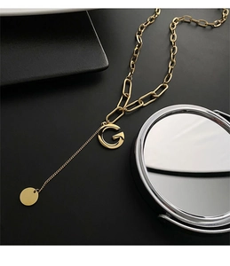 Macro detail of gold G letter pendant on heavy chain necklace with a light luxury finish