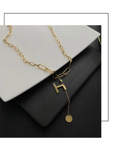 Detail view of bold gold link chain featuring a large H pendant and circular charm