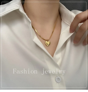 Close-up of a heart pendant gold necklace on a woman wearing a white silk shirt