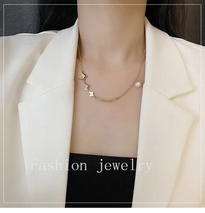Detail of 18k gold butterfly necklace with pearl accent worn on a white blazer