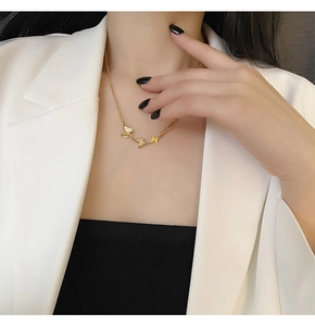 Three gold butterfly pendants on an elegant chain worn by a model in a white blazer