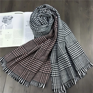 Detail of houndstooth cashmere scarf with fringe on a wooden floor next to a magazine