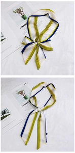 Detail of slim striped scarf tied in a bow on a white linen surface with minimalist decor