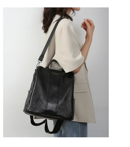 Detail view of black textured leather anti-theft backpack showing side pocket and strap