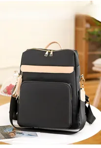 Détail du sac à dos en nylon noir avec accents marron et pompon décoratif sur une table blanche