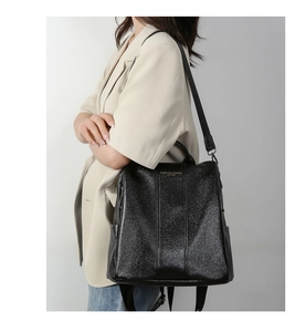 Detail of black wrinkled leather backpack featuring glossy texture and gold logo lettering