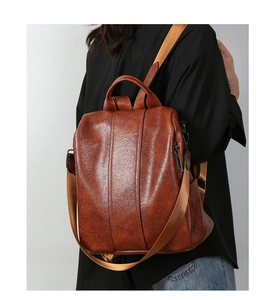 Side view of brown pebbled leather backpack showing the adjustable nylon straps on a model