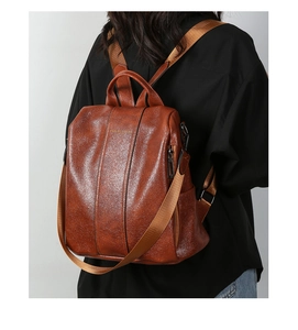 Detailed view of brown glossy leather backpack with vertical stitching and gold logo
