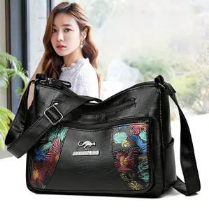 Close-up of black leather crossbody bag featuring colorful floral embroidery and metal logo