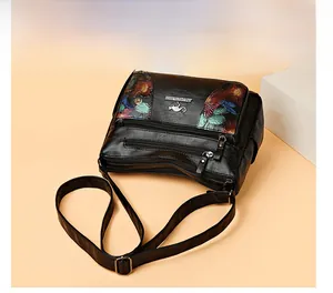 Detail view of black faux leather crossbody bag with floral embroidery and multi-zipper pockets