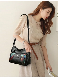 Model wearing a black soft leather shoulder bag with colorful floral print and multiple zippers