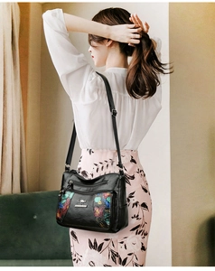 Detailed close-up of a black leather shoulder bag with colorful tropical floral prints
