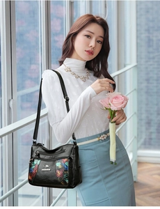 Detail of floral printed black leather crossbody bag with multiple zip pockets and metal logo